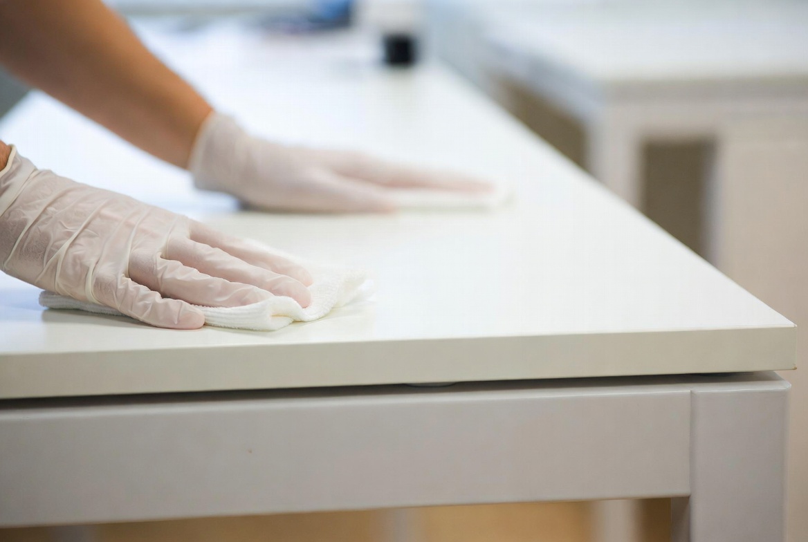 Close-up of gloved hands detail cleaning a commercial desk surface